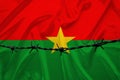 National flag of Burkina Faso on satin, iron barbed wire, concept of war, revolution, an armed uprising in the country, shootout