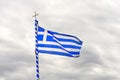 The National Flag Of Greece Looks Like 9 White And Blue Stripes With A Cross On A Background Of A Gray Cloudy Sky.