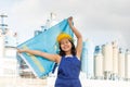 National flag of Kazakhstan in the hands of girl in overalls against background of modern metallurgical plant