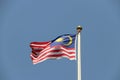 National flag of Malaysia on bright blue sky background. Blown away by wind. Royalty Free Stock Photo