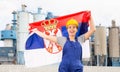 National flag of Serbia in the hands of girl in overalls against background of modern metallurgical plant