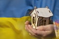 The national flag of Ukraine is yellow-blue on the background of children's hands holding a wooden small house