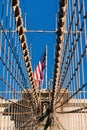 The national flag of United States of America winding on top of Brooklyn Bridge landmark from Manhattan.