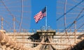 The national flag of United States of America winding on top of Brooklyn Bridge landmark from Manhattan.