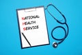 National health service (NHS). Clipboard with text, pen and stethoscope on light blue background, top view Royalty Free Stock Photo