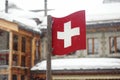 National swiss flag white cross on red background on street of small town in Alps, Switzerland. Winter vacation Royalty Free Stock Photo