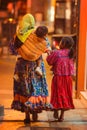 Native poor Indigenous lady and children in traditional colorful dress in city at night, Mexico, America