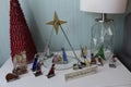 Nativity scene made of colored glass and metal frames on a small end table next to a lamp and stylized Christmas tree