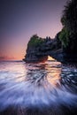 Natural arch. Batu Bolong temple on the rock during sunset. Seascape background. Motion milky waves on black sand beach. Copy Royalty Free Stock Photo