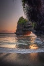 Natural arch. Batu Bolong temple on the rock during sunset. Seascape background. Motion milky waves on black sand beach. Copy Royalty Free Stock Photo