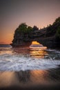 Natural arch. Batu Bolong temple on the rock during sunset. Seascape background. Motion milky waves on black sand beach. Copy Royalty Free Stock Photo