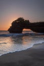 Natural arch. Batu Bolong temple on the rock during sunset. Seascape background. Motion milky waves on black sand beach. Copy Royalty Free Stock Photo