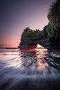 Natural arch. Batu Bolong temple on the rock during sunset. Seascape background. Motion milky waves on black sand beach. Copy Royalty Free Stock Photo