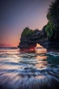 Natural arch. Batu Bolong temple on the rock during sunset. Seascape background. Motion milky waves on black sand beach. Copy Royalty Free Stock Photo