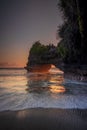 Natural arch. Batu Bolong temple on the rock during sunset. Seascape background. Motion milky waves on black sand beach. Copy Royalty Free Stock Photo