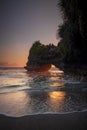 Natural arch. Batu Bolong temple on the rock during sunset. Seascape background. Motion milky waves on black sand beach. Copy Royalty Free Stock Photo