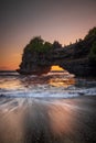 Natural arch. Batu Bolong temple on the rock during sunset. Seascape background. Motion milky waves on black sand beach. Copy Royalty Free Stock Photo