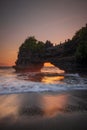 Natural arch. Batu Bolong temple on the rock during sunset. Seascape background. Motion milky waves on black sand beach. Copy Royalty Free Stock Photo