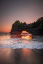 Natural arch. Batu Bolong temple on the rock during sunset. Seascape background. Motion milky waves on black sand beach. Copy Royalty Free Stock Photo