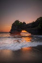 Natural arch. Batu Bolong temple on the rock during sunset. Seascape background. Motion milky waves on black sand beach. Copy Royalty Free Stock Photo