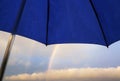 Natural background with a blue umbrella in raindrops and a rainbow under it in the distance on the horizon of a clear sky Royalty Free Stock Photo