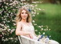 Natural beauty adult woman in white dress with bouquet of wild flowers is sitting in a chair in a blooming garden, enjoying the