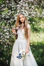 Natural beauty woman in white dress with a bouquet of wild flowers walks in the summer garden, enjoying the blooming spring nature Royalty Free Stock Photo