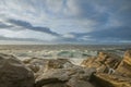 Natural breakwater receiving the onslaught of the waves with views of some islands on the horizon at sunset with the sky full of