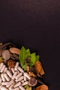 Natural capsules, green herbs and assorted spices on black background with copy space. Herbal extracts concept