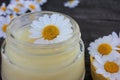 Natural chamomile face cream and fresh daisy flowers on dark rustic wooden background. Homemade beauty product.