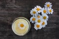 Natural chamomile face cream and fresh daisy flowers on dark rustic wooden background. Homemade beauty product. Royalty Free Stock Photo