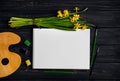 Sketchbook, watercolor and brushes on black wooden table with bouquet of daffodils. Flat lay, top view