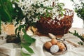 Natural Easter eggs painted with wax on vintage plate on background of wicker basket, white spring flowers and greenery on wooden