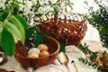 Natural Easter eggs painted with wax in wooden bowl on background of wicker basket, white spring flowers and greenery on wooden Royalty Free Stock Photo