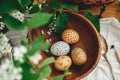 Natural Easter eggs painted with wax in wooden bowl on background of wicker basket and white spring flowers on wooden table. Happy Royalty Free Stock Photo
