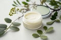 Natural face cream in petri dish on a white table and plant branches, copy space