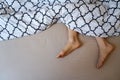 Natural female feet in bed with patterned bed sheet.