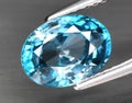 Natural gemstone blue zircon in tongs on a gray background Royalty Free Stock Photo