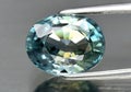 Natural gemstone blue zircon in tweezers on a gray background Royalty Free Stock Photo