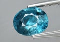 Natural gemstone blue zircon in tweezers on a gray background Royalty Free Stock Photo