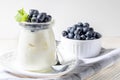 Natural homemade yogurt in glass jar with fresh forest blueberries on kitchen napkin on white