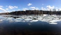 Natural landscape with ice floes adrift on the spring river and forest trees on opposite bank under clouds on blue sky reflected i Royalty Free Stock Photo