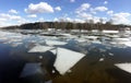 Natural landscape with ice floes adrift on the spring river and forest trees on opposite bank under clouds on blue sky reflected i Royalty Free Stock Photo