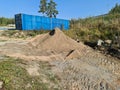 Natural landscape view showing sand pile near big blue container. on clear blue sky background.