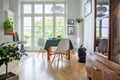 Natural light coming through glass door from balcony into a stylish kitchen room interior with white chairs around a wooden dining