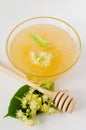 Natural linden honey in a transparent bowl and branch linden blossom on a white wooden background.