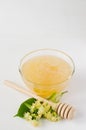 Natural linden honey in a transparent bowl and branch linden blossom on a white wooden background.