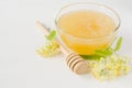 Natural linden honey in a transparent bowl and linden blossom on a white wooden background.