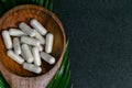 Natural medicine concept - Herbal capsules on wood spoon with leaf on dark background