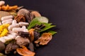 Natural medicine concept. scattered different spices, herbs and herbal capsules with green leaves on black ground Royalty Free Stock Photo